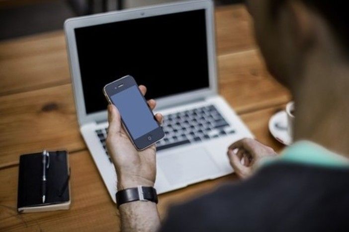 Persona con in mano un cellulare e un pc